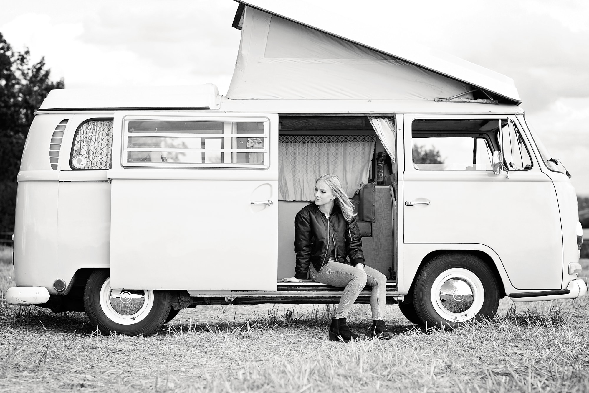 Vintage campervan with young woman sitting outside, outdoor photography, lifestyle, travel, black and white image.