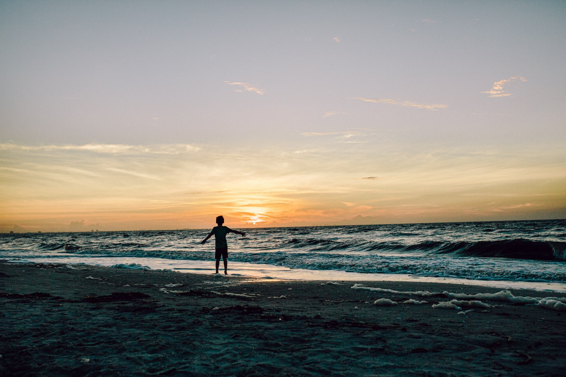 Sunset at the beach with child playing in the waves, capturing scenic coastal photography.