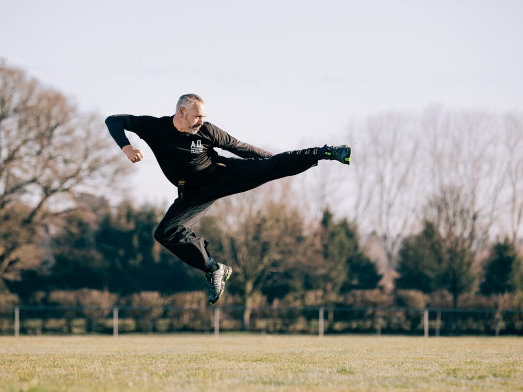 Dynamic martial arts kick performed outdoors, showcasing strength and agility in green field.
