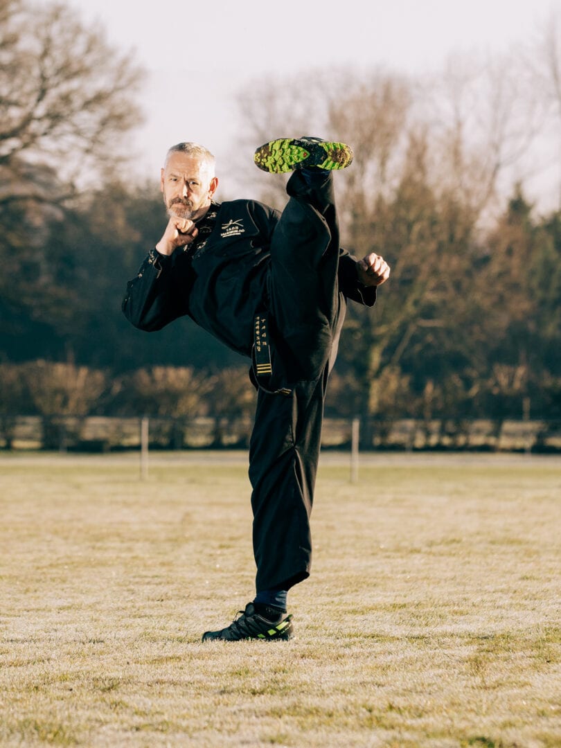 Dynamic martial artist performing high kick outdoors, showcasing discipline and skill.