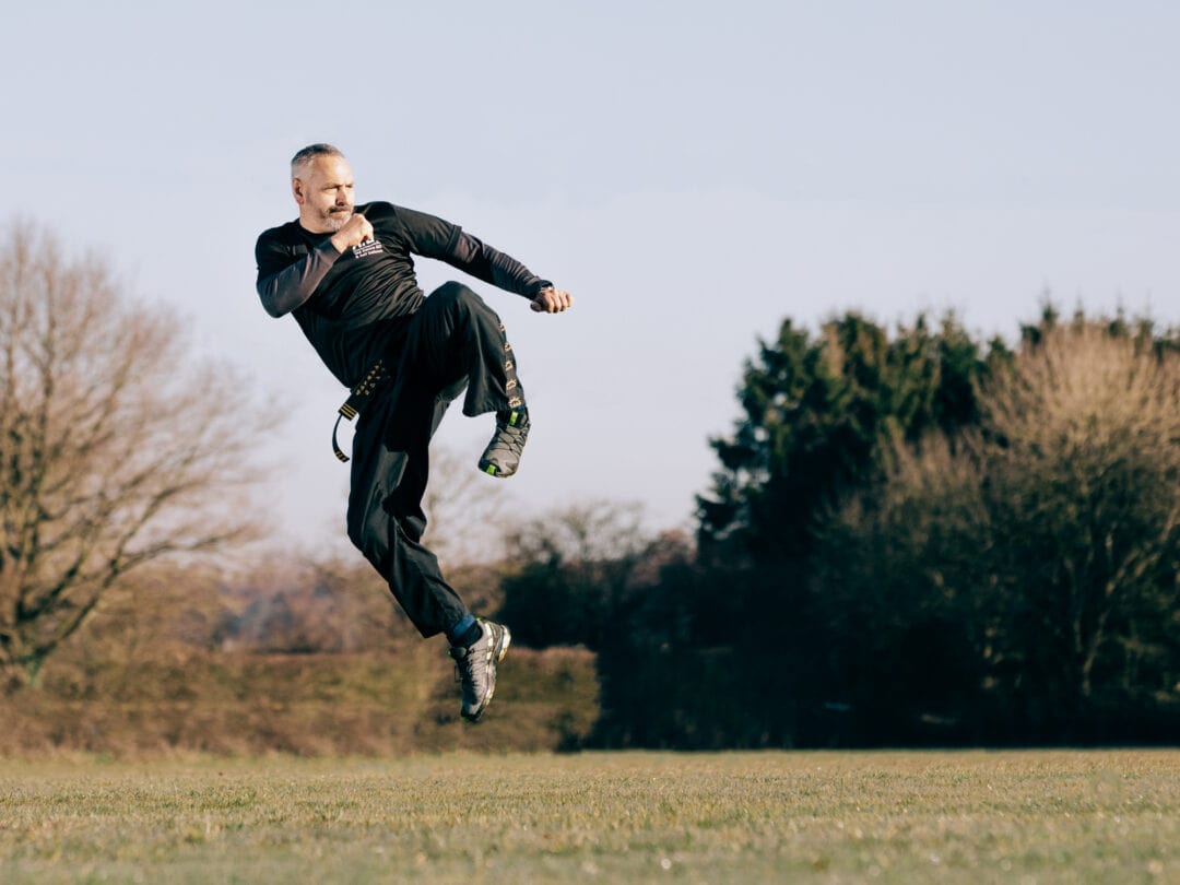 Dynamic martial arts kick captured outdoors during daylight.