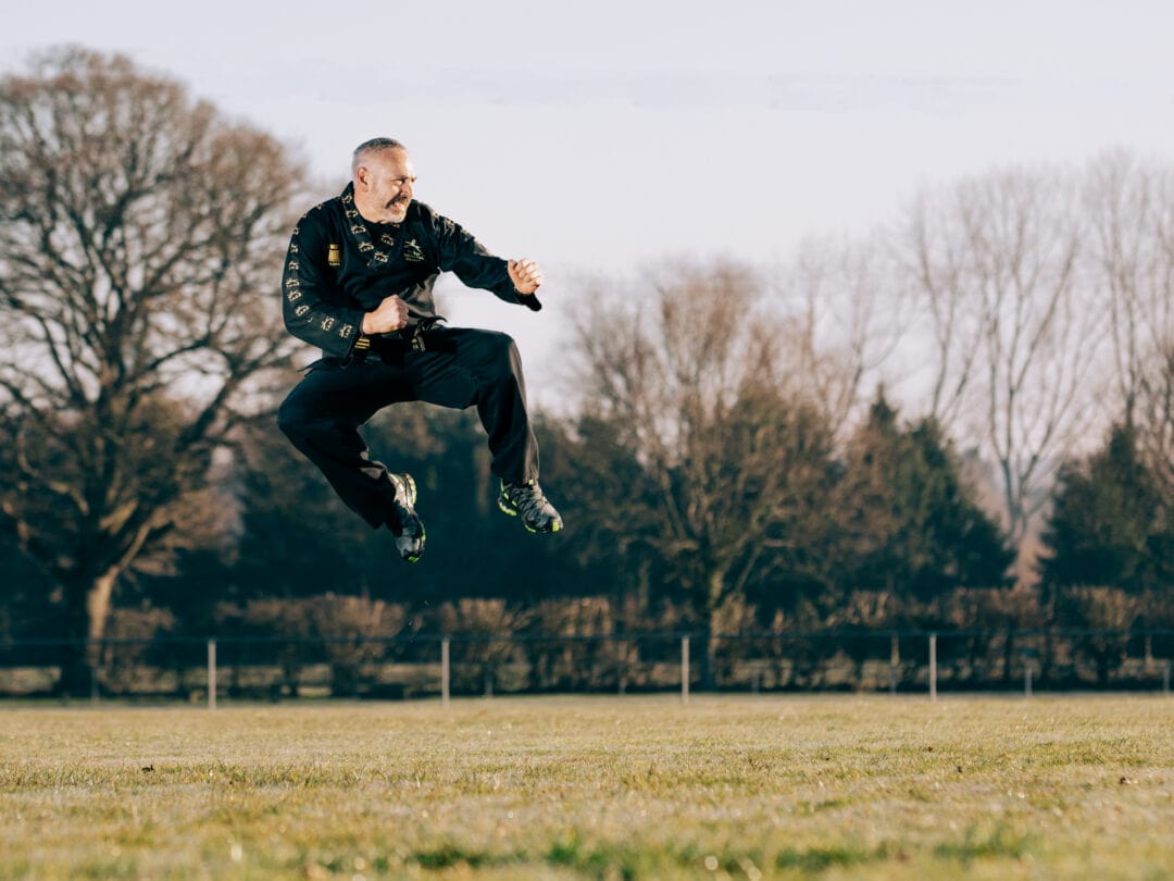 Jumping martial artist in outdoor park, professional sports photography, dynamic action shot.