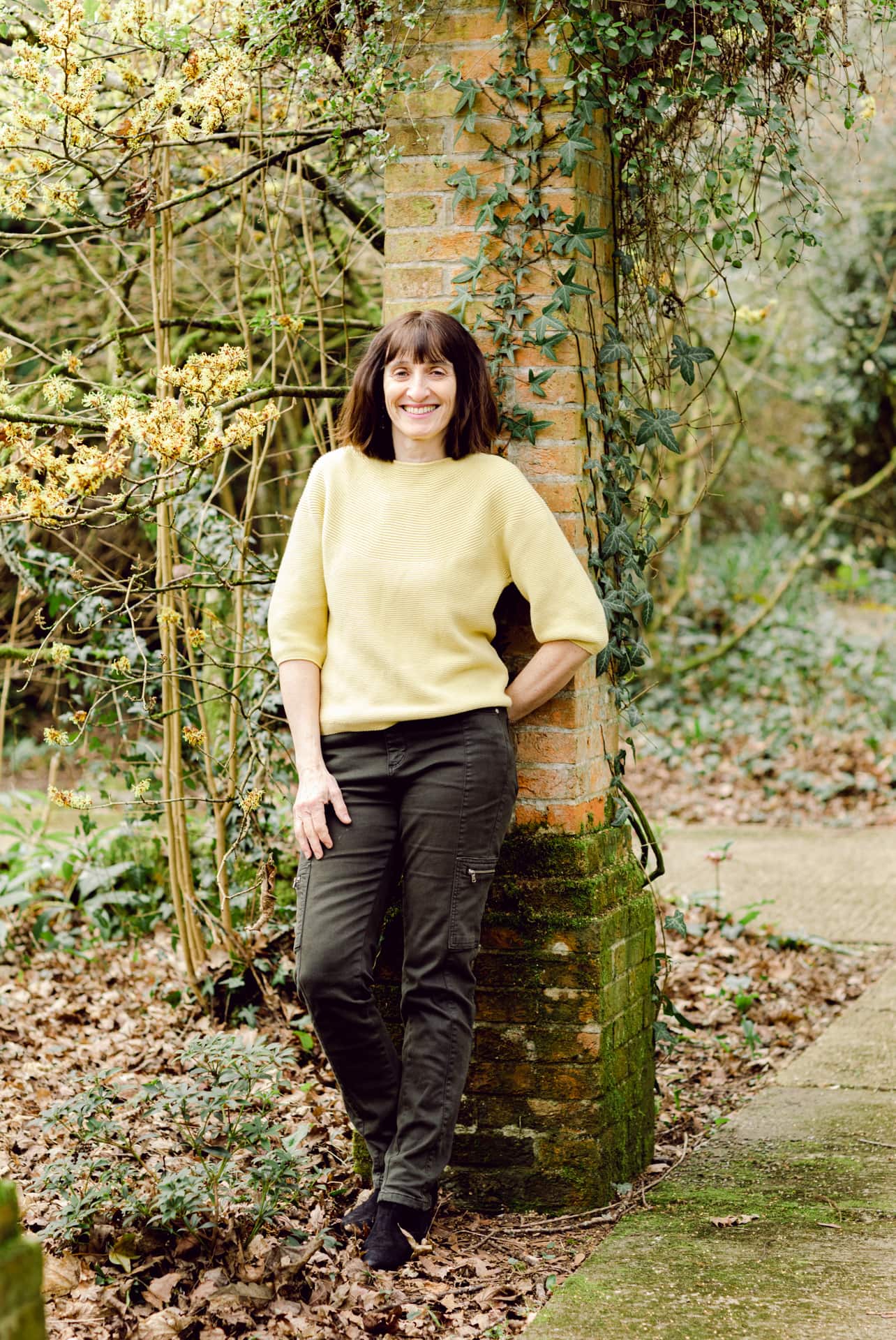 Elegant woman smiling outdoors with lush garden backdrop - professional portrait photography.