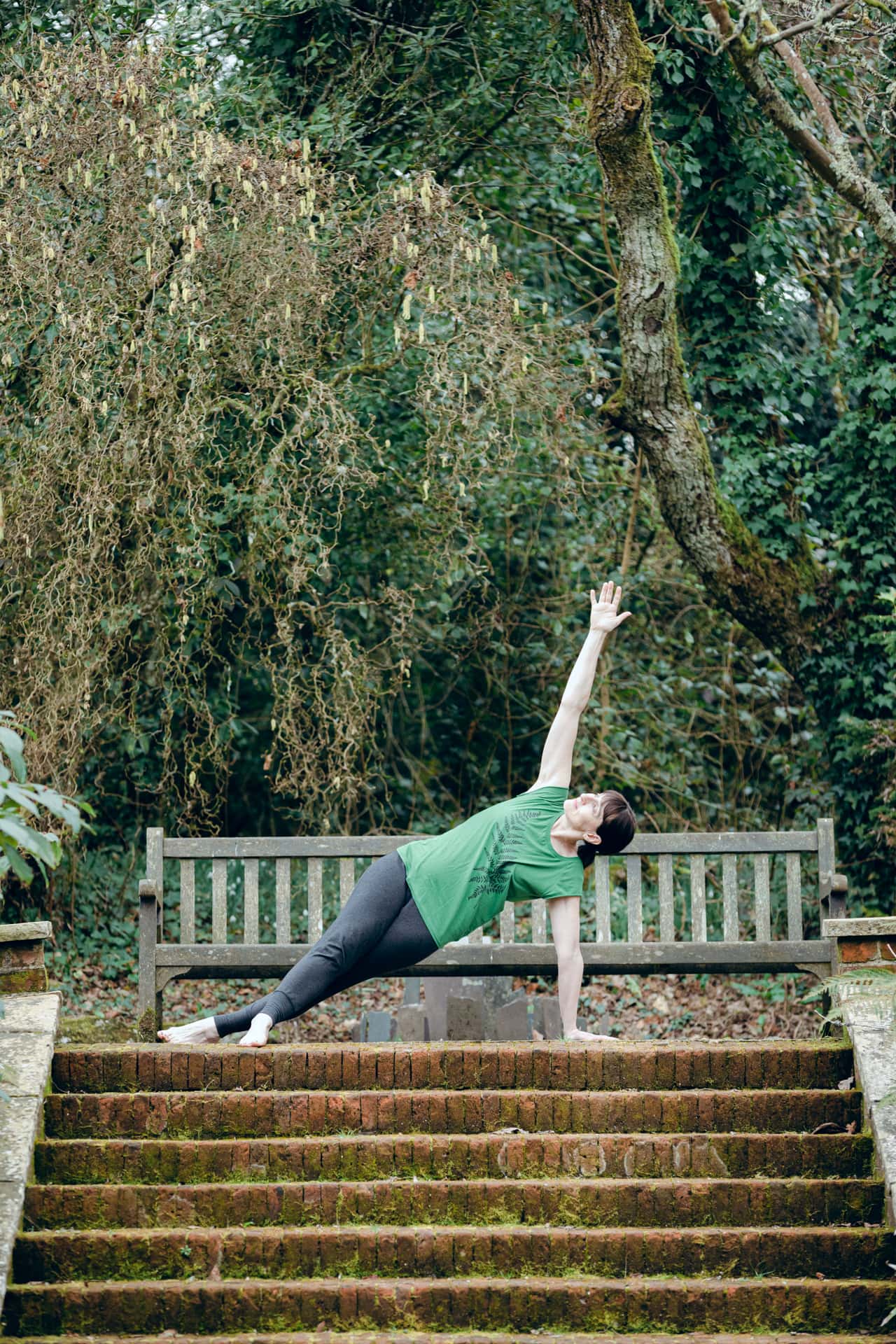 Young woman practising yoga outdoors on steps in a park, performing side plank pose.
