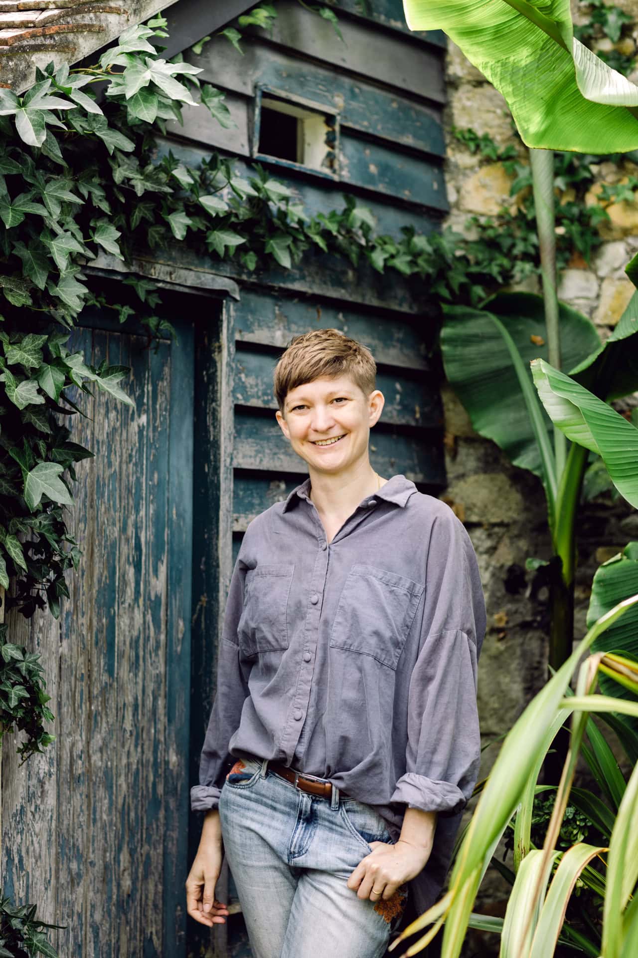 Vintage garden shed portrait of woman in denim and grey shirt, lush greenery, botanical photography, outdoor lifestyle, natural light, Jo Worthington photography.