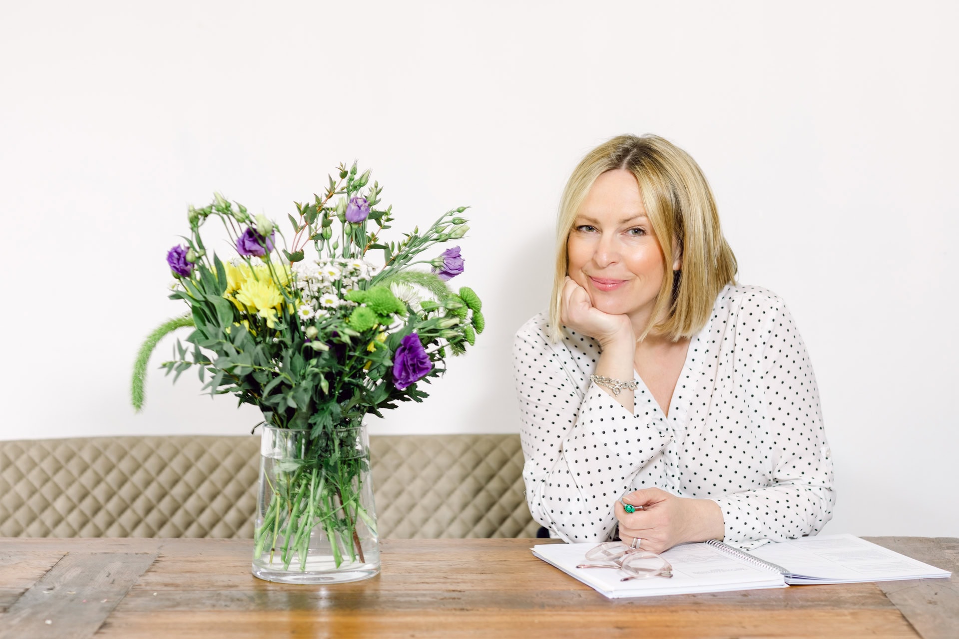 Vibrant flower bouquet with woman in polka dot blouse sitting at wooden table.