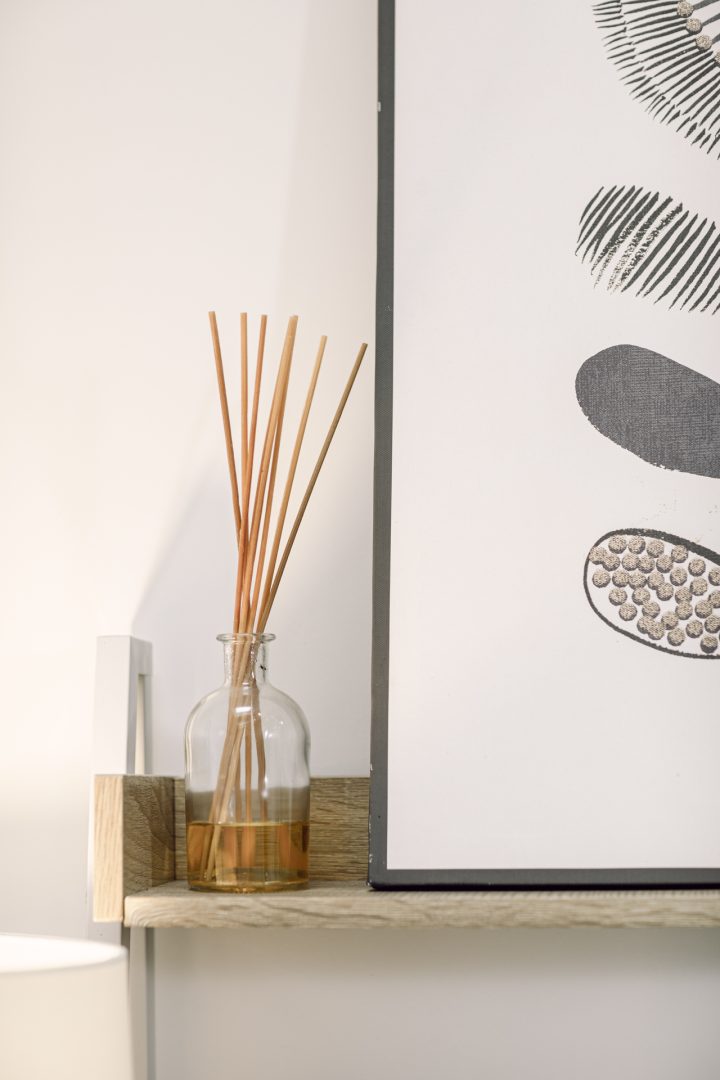 Rod diffuser sticks in a glass jar on a wooden shelf, modern minimalist interior decor, black and white botanical artwork.