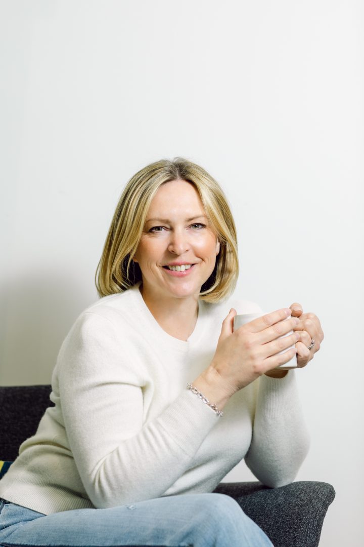 Professional woman holding coffee mug, natural light, casual portrait photography.