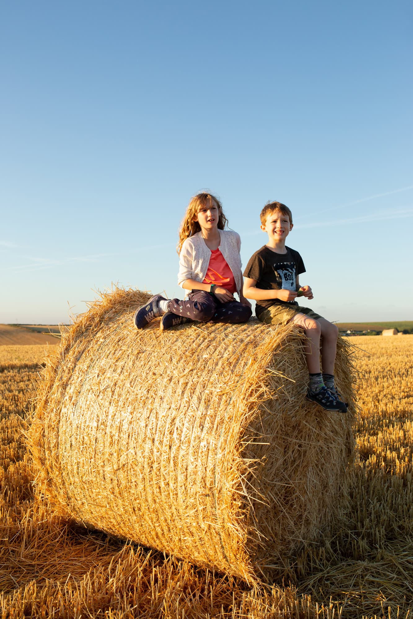 Vibrant outdoor photography of children sitting on hay bale during sunset, capturing joyful moments in rural landscape.