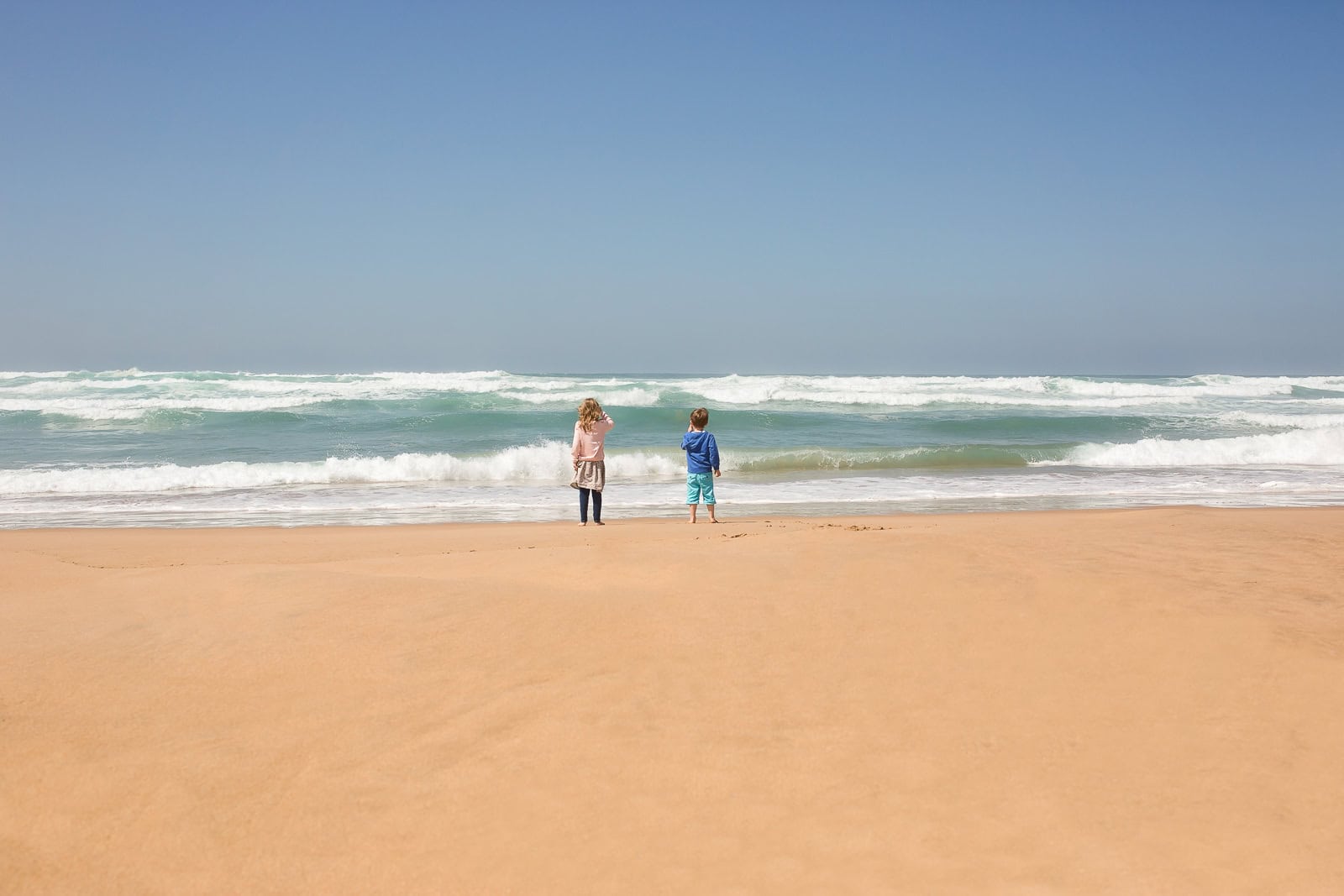 Children playing on sandy beach with waves and blue sky in the background.