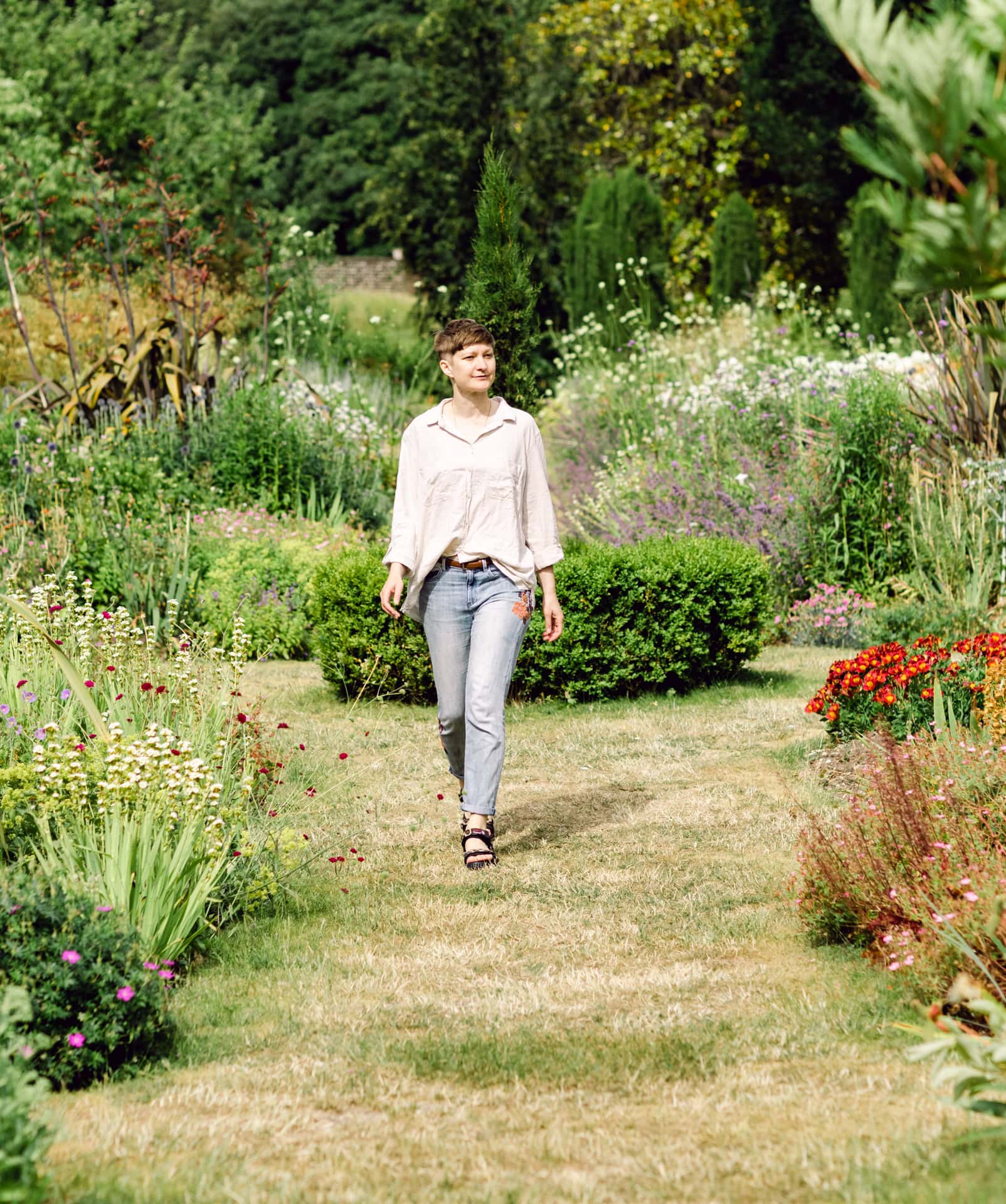 Vibrant garden pathway with a woman enjoying floral surroundings, capturing outdoor portrait photography in a lush garden setting.